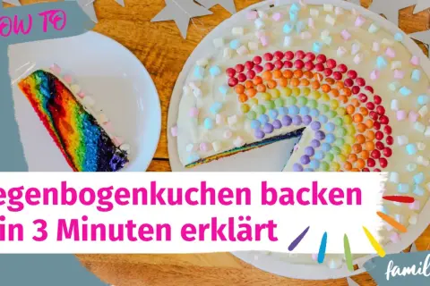 Ein bunter Regenbogenkuchen, verziert mit Marshmallows und bunten Smarties. Ein Stück ist bereits angeschnitten.