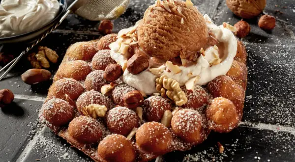 Bubble Eis auf einem Waffel-Snack, bestreut mit Puderzucker und garniert mit Nüssen und einer Kugel Eis.
