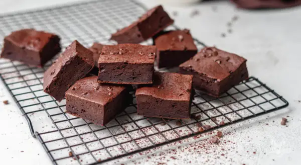 Saftige low carb brownies, bestreut mit Kakaopulver und Schokostückchen, auf einem Kuchengitter.