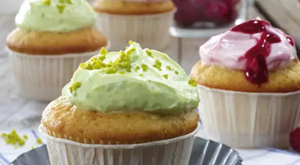 Zwei Cupcakes mit cremiger, grüner Pistazien-Frosting und ein weiterer mit rosa Beeren-Frosting.