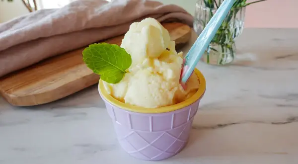 Ein cremiges Ananas Eis in einem lila Becher, garniert mit Minze. Perfekt für heiße Tage!