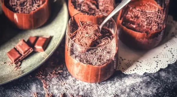 Schokoladenmousse ohne Ei, garniert mit Schokostreuseln. Ein Löffel hebt eine Portion aus dem Glas.