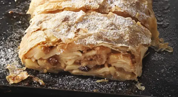 Ein saftiger Apfelstrudel, bestäubt mit Puderzucker, wartet darauf, nach diesem Rezept gebacken zu werden.