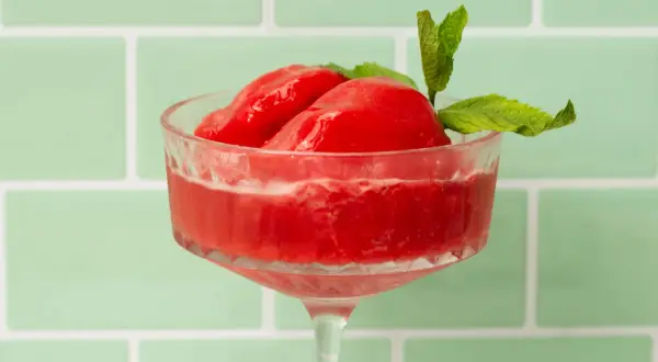 Erfrischendes Wassermelonen Sorbet in einem eleganten Glas, garniert mit Minze. Perfekt für heiße Tage.