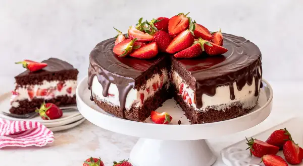 Eine saftige Yogurette Torte mit Schokoladenglasur und frischen Erdbeeren, ein Stück davon ist bereits angeschnitten.