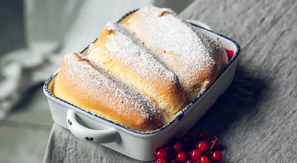 Drei goldbraune Salzburger Nockerl, mit Puderzucker bestäubt, in einer Auflaufform, daneben rote Johannisbeeren.