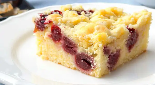 Ein saftiges Stück Kirsch-Streuselkuchen vom Blech, mit vielen Kirschen und knusprigen Streuseln, auf einem weißen Teller.