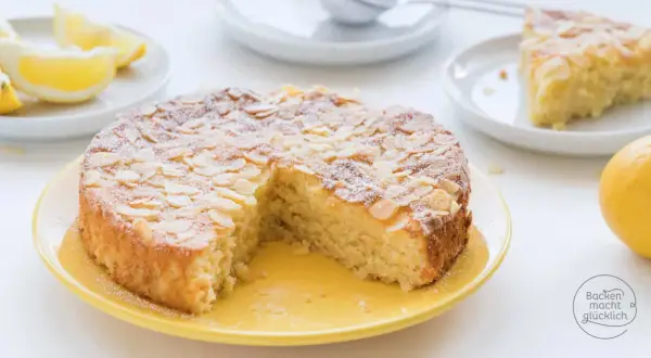 Saftiger mandelkuchen rezept, bestäubt mit Puderzucker und Mandelsplittern, daneben Zitronenspalten und eine ganze Zitrone.
