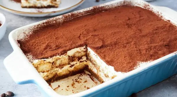 Ein cremiges Tiramisu, perfekt für ein tiramisu rezept ohne alkohol. Mit Kakaopulver bestäubt und in einer blauen Auflaufform serviert.