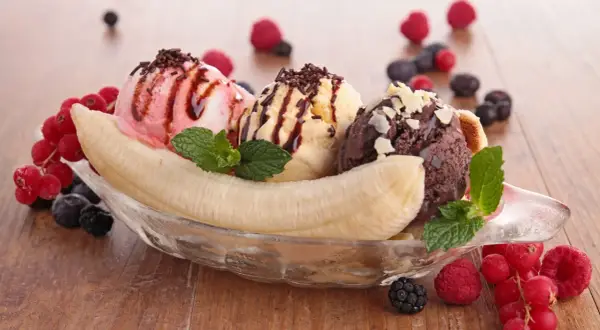 Ein köstlicher Bananensplit Eis mit drei Kugeln Eis, garniert mit Beeren und Minze.