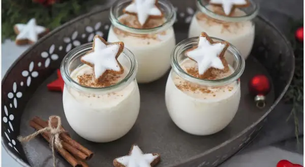 Vier Gläser mit cremigen Parfait-Rezepten im Glas, garniert mit Zimt und Sternenplätzchen. Weihnachtliche Deko mit Zimtstangen und Kugeln.