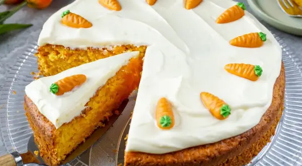 Ein saftiger Karottenkuchen mit weißem Zuckerguss und kleinen Marzipanmöhren. Perfekt für ein Osterkuchen Rezept!