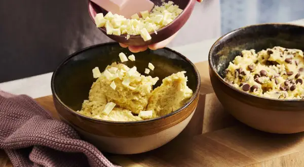 Zutaten für ein Crumble Cookie Rezept werden in Schüsseln gegeben: Teig mit Schokostückchen und weißer Schokolade.