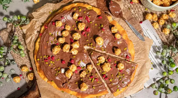 Eine köstliche Nutella Pizza, belegt mit karamellisiertem Popcorn und gehackten Pistazien, bereit zum Genießen.