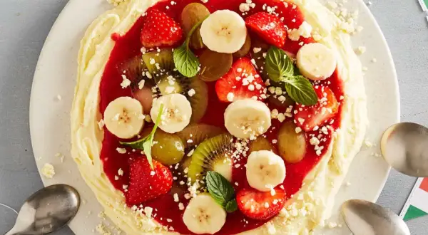 Fruchtige eis pizza mit Erdbeeren, Bananen, Kiwi und Trauben auf cremigem Boden, garniert mit Minze.