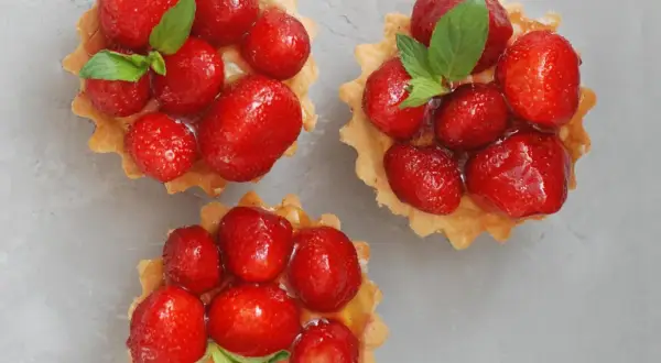 Drei köstliche Erdbeer Tartelettes, garniert mit frischer Minze, auf grauem Untergrund.