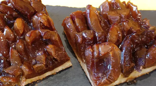 Zwei Stücke saftiger Zwetschgenkuchen vom Blech, glänzend und karamellisiert, auf dunkler Platte angerichtet.
