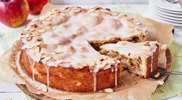 Ein köstlicher gedeckter Apfelkuchen mit zarter Glasur und Mandelblättchen, daneben ein Stück Apfelmus.