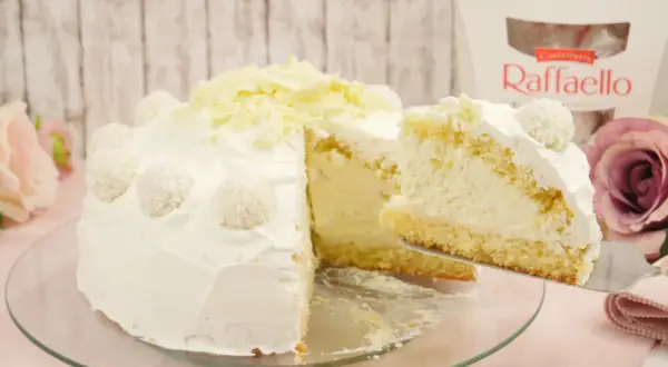 Eine köstliche Raffaello Torte, verziert mit Kokosraspeln und weißer Schokolade. Ein Stück wird gerade serviert.