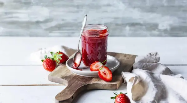 Frische Erdbeeren und selbstgemachte Erdbeermarmelade aus dem Thermomix auf einem Holzbrett.