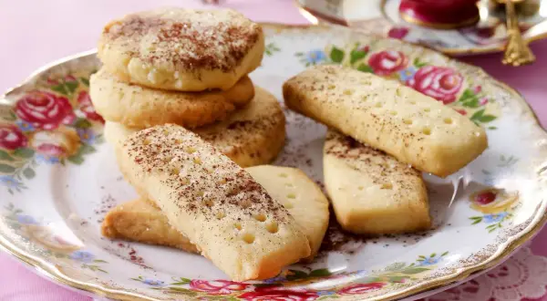Leckeres Shortbread-Rezept: goldbraune Kekse, rund und rechteckig, mit Zimt und Zucker bestreut, auf einem floralen Teller.