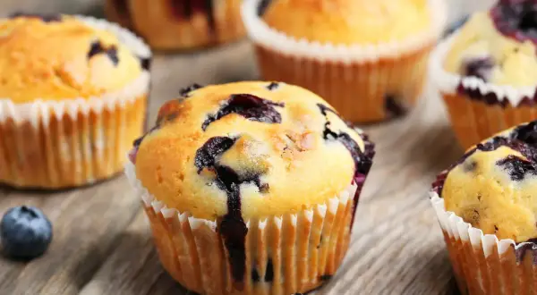 Saftige Blaubeermuffins, perfekt für ein Blaubeermuffins Rezept. Frisch gebacken und auf rustikalem Holz angerichtet.