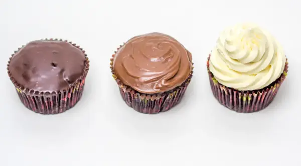 Drei Cupcakes: einer mit dunkler Ganache, einer mit Milchschokoladen-Ganache und einer mit weißer Creme. Perfekt für ein schnelles Ganache Rezept.