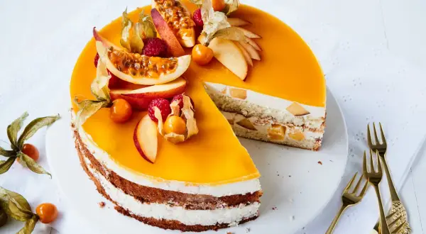 Eine köstliche Pfirsich Maracuja Torte, dekoriert mit frischen Früchten und Physalis. Ein Stück ist bereits angeschnitten.