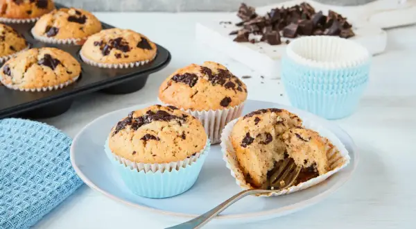 Schokoladenmuffins, frisch gebacken nach einem einfachen Muffins Rezept. Ein Muffin ist angeschnitten und zeigt die saftige Krume.