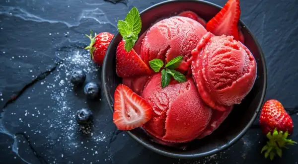 Schüssel mit erfrischendem Erdbeer-Sorbet-Eis, garniert mit frischen Erdbeeren und Minze, daneben Blaubeeren.