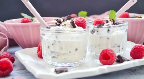 Zwei Gläser mit cremigem Dessert, garniert mit Himbeeren und Schokostückchen. Ein leckeres Herrencreme Rezept zum Nachmachen.