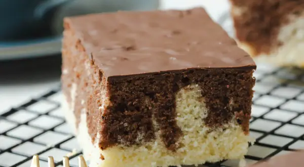 Ein Stück saftiger Marmorkuchen vom Blech mit Schokoladenglasur auf einem Kuchengitter.