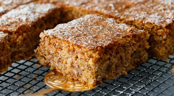 Ein saftiger karottenkuchen glutenfrei, bestäubt mit Puderzucker, wird auf einem Gitter präsentiert.