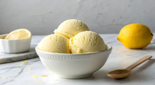 Erfrischendes Limoncello Eis in einer Schale, daneben eine Zitrone und ein Löffel.