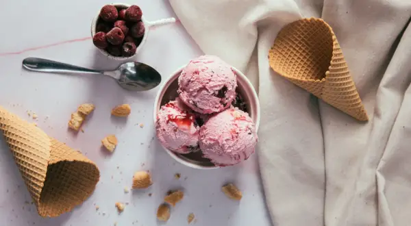 Schüssel mit rosa Eiskugeln, Kirschen und Waffelhörnchen. Ein süßer Genuss, der trotz der Kalorien verlockt.