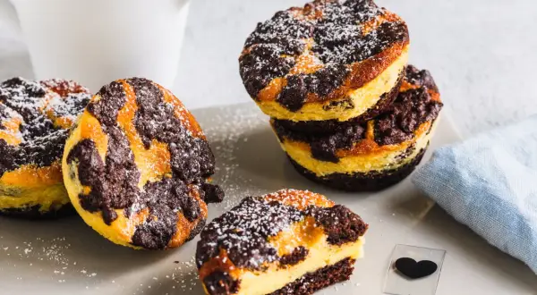 Leckere zupfkuchen muffins mit Puderzucker bestäubt, daneben ein Milchkännchen und ein blaues Tuch.