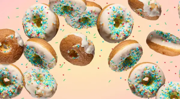 Bunte Donuts mit weißer Glasur und Streuseln schweben im Bild. Ein köstliches Rezept für selbstgemachte Donuts.