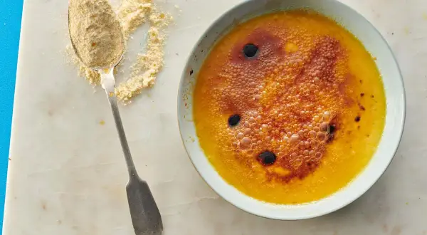 Creme brulee mit karamellisierter Zuckerkruste und Bläschen, daneben ein Löffel mit feinem Zucker.