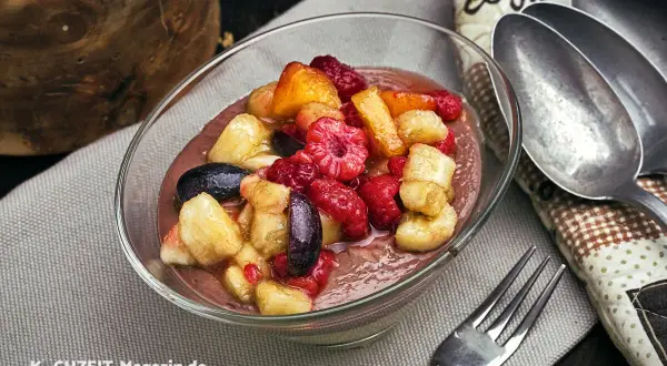 Schüssel mit cremigem Dessert und frischem Obstsalat aus Himbeeren, Bananen und Aprikosen. Perfekt für ein leichtes obstsalat rezept.