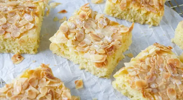 Saftiger Buttermilch Kuchen mit knusprigen Mandelblättchen und Zucker bestreut, auf Backpapier und einem Gitterrost.