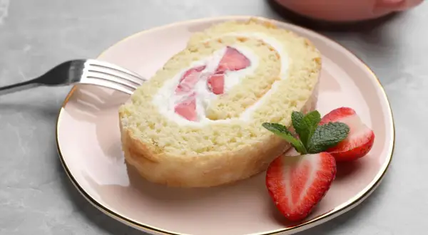 Ein Stück Biskuitrolle mit Erdbeeren und Sahne, perfekt für ein leichtes Dessert. Dieses Biskuitrolle Rezept ist ein Genuss!