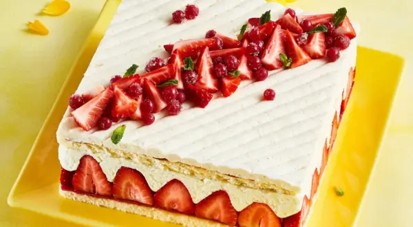 Rechteckiger Kuchen mit Erdbeeren und roter Johannisbeere auf leichter Erdbeer-Buttercreme, verziert mit Minze.