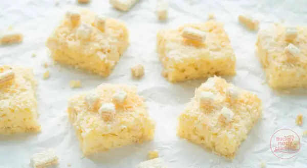 Saftige Stücke Buttermilch Kokos Kuchen, bestreut mit Kokosraspeln und kleinen weißen Würfeln, verlocken zum Genuss.