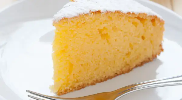 Ein saftiges Stück Vanille Kuchen, bestäubt mit Puderzucker, wartet auf dem Teller neben einer Gabel.