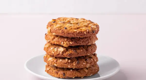 Ein Stapel knuspriger Kekse ohne Zucker, verfeinert mit Haferflocken und Samen, auf einem weißen Teller.
