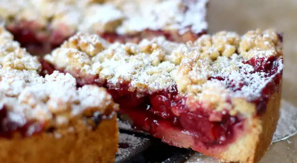 Saftiger kirschkuchen mit streusel, bestäubt mit Puderzucker. Ein Stück wurde herausgeschnitten, um die roten Kirschen zu enthüllen.