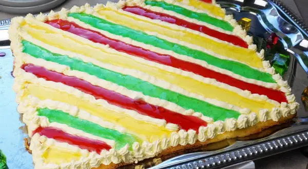 Bunte Philadelphia Torte mit Waldmeister-Aroma, dekoriert mit Sahnetuffs und roten Fruchtstreifen.