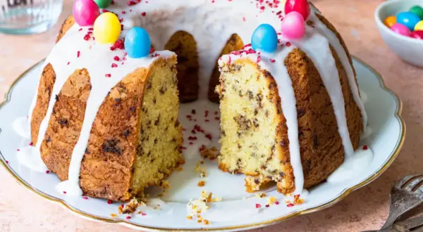Ein Gugelhupf mit Schokoladenstückchen, Zuckerguss und bunten Ostereiern. Dieses Gugelhupf Rezept ist perfekt für Ostern.