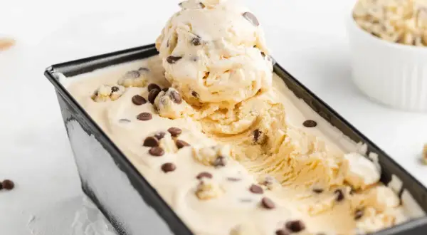 Cremiges Cookie Dough Eis mit Schokoladenstückchen in einer schwarzen Form, eine Kugel ist herausgenommen.