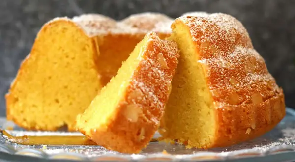 Ein saftiger Kuchen mit vielen Eiern, bestäubt mit Puderzucker, auf einem Glasständer.